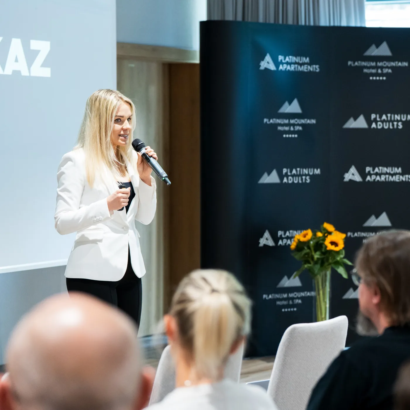 Ewa Wilmanowicz z mikrofonem podczas wydarzenia, na tle ścianki Platinum Apartments